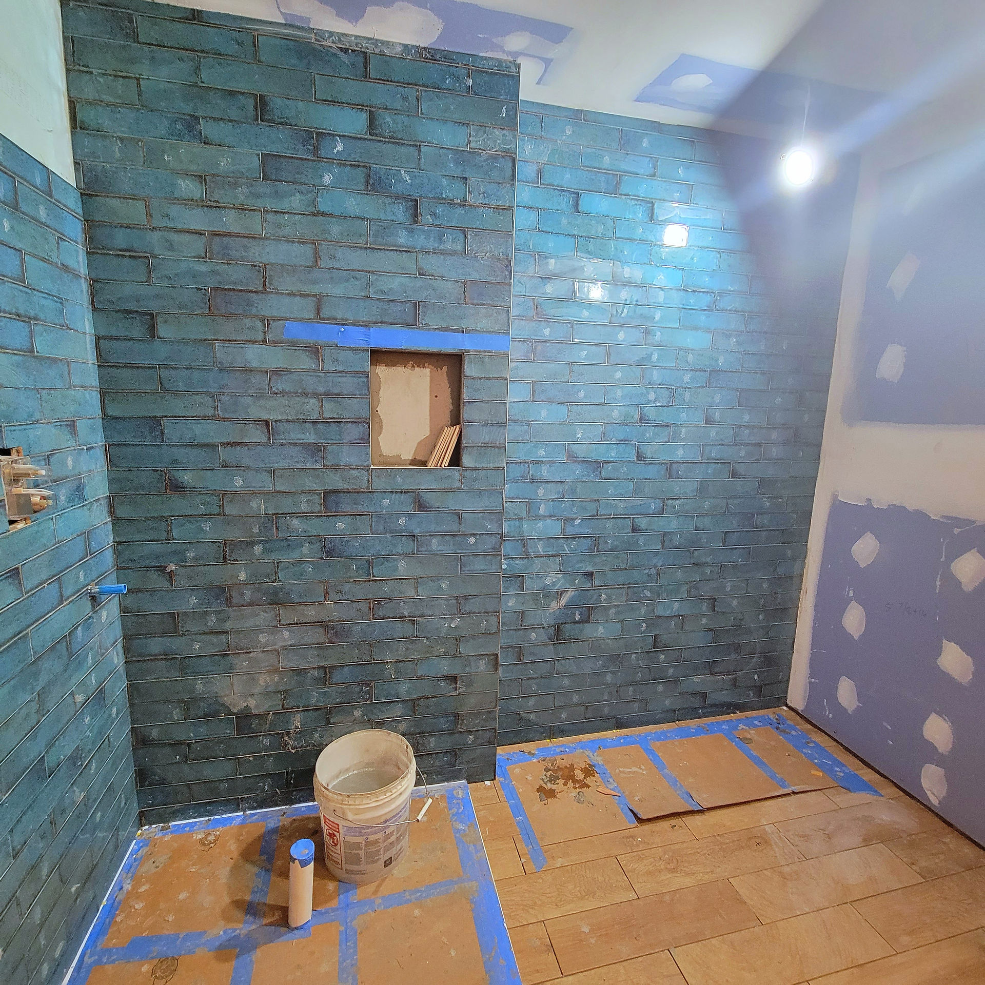 Completed walls tiled with blue textured tiles in shower and tub areas