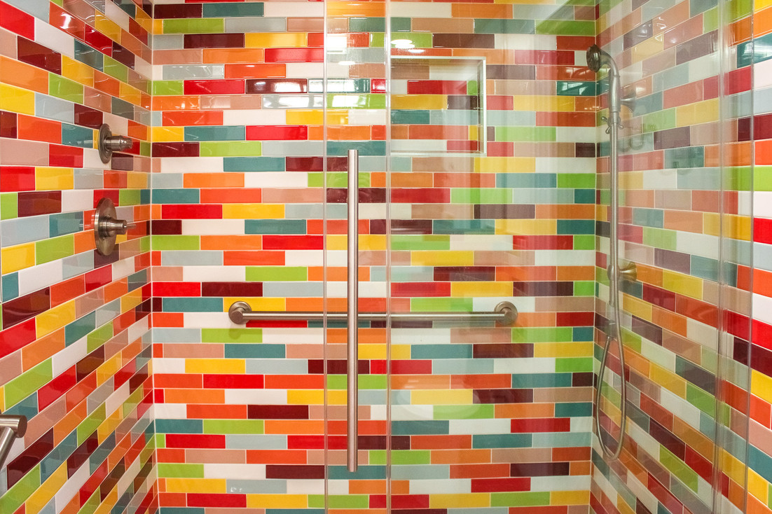 Multi-colored, glossy tile shower surround is stunning with floating glass door in the Colorful Flashback bathroom by Barrett Home Renovations