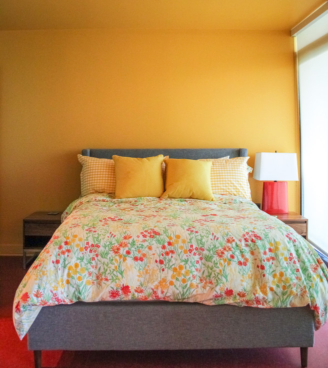 Red and yellow flowers on the comforter with bright yellow throw pillow in the bedroom living room of the Colorful Flashback Apartment by Barrett Home Renovations