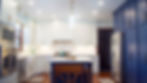 navy blue cabinets from head to toe on right, and white shiny kitchen with a oven stack on left