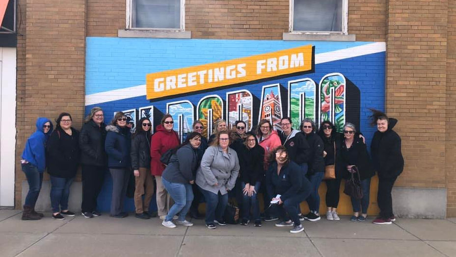 Group photo in front of mural reading Greetings from Trinidad, Colorado.