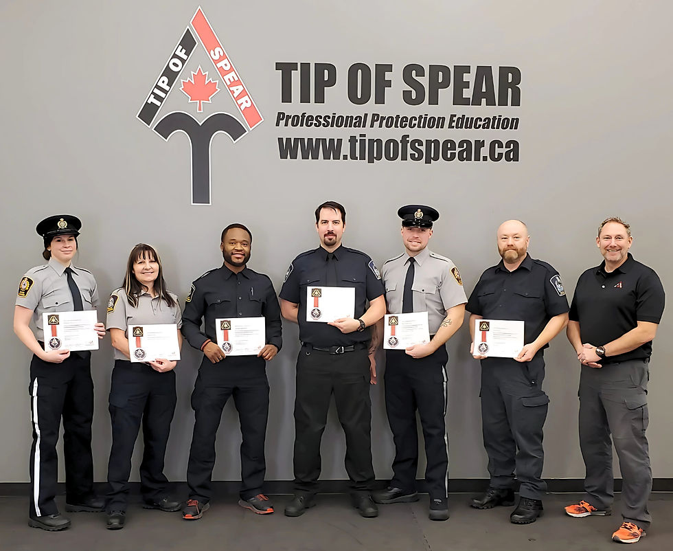 Six uniformed individuals hold certificates, standing in front of a wall reading "TIP OF SPEAR." They appear proud, with a professional mood.