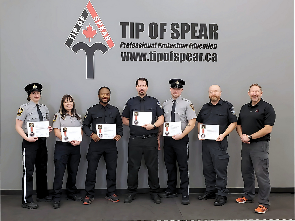 Seven people in uniforms pose with certificates against a gray wall with "TIP OF SPEAR Professional Protection Education" text.