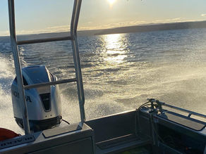 Looking out of the back of the boat with water spray being displaced by the Honda BF250 engine. The sun has started setting creating a sparkling trail of light on the water.