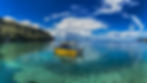 Yellow boat on clear turquoise water between green cliffs under a blue sky with clouds. Text on boat reads "Adventures." Serene atmosphere.