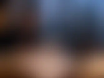 Homem concentrado analisa documentos à mesa com laptop e livros, em escritório à noite, com skyline iluminado ao fundo.