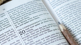 Open Bible with visible Ten Commandments text and a pencil resting on the page, in a quiet reading scene.