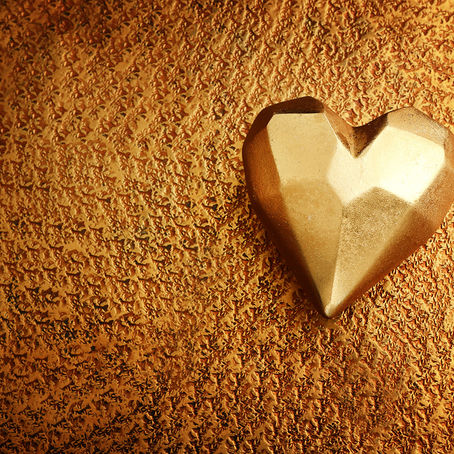 Golden angular heart sculpture resting on textured golden surface
