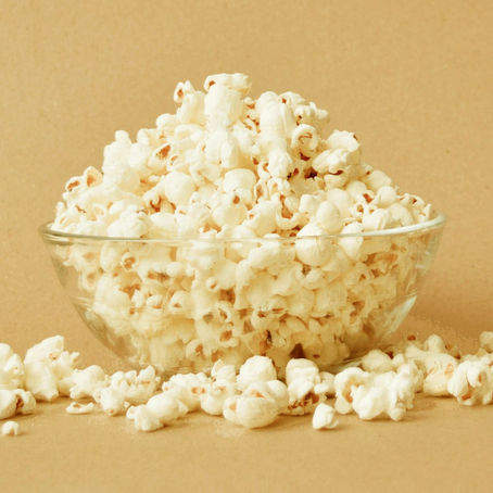 Overfilled bowl of popcorn on a beige backdrop with popcorn spilling over