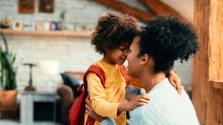 Mother and daughter share a tender forehead touch in a cozy living room with wood beams and soft decor.