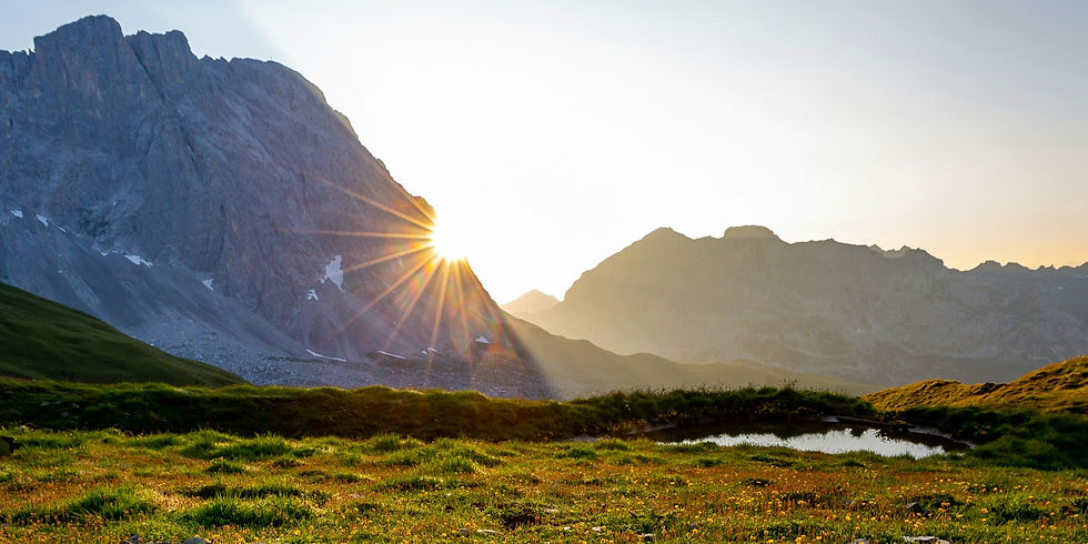 Sunlight peering over a mountain and shining onto a grassy field