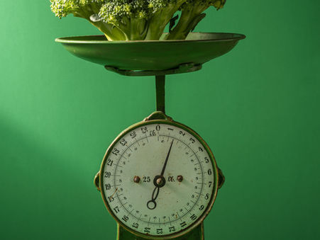 A set of green scales with broccoli in the basket, against a green wall