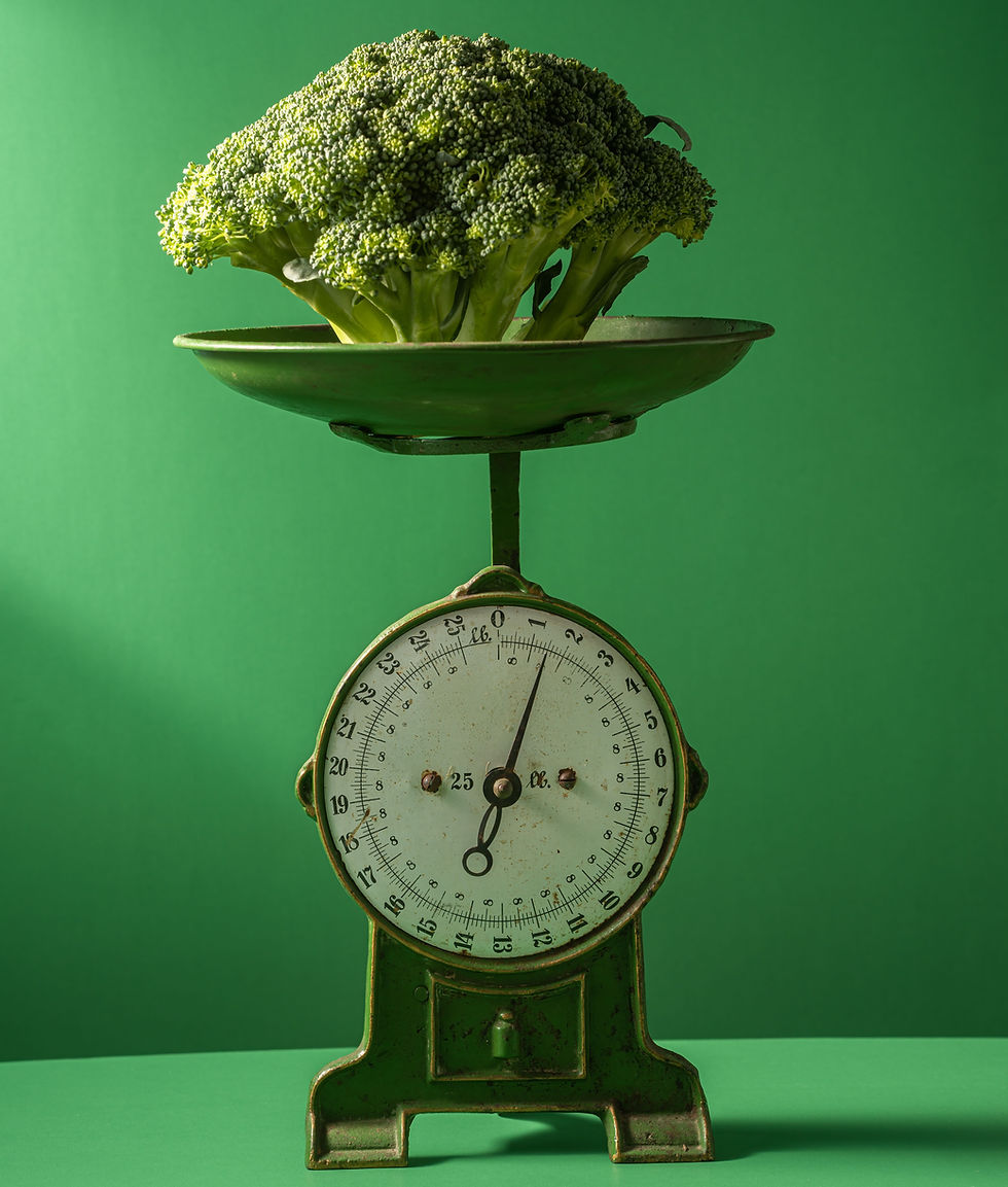 A set of green scales with broccoli in the basket, against a green wall