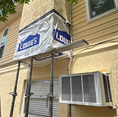 Building exterior with scaffolding, Lowe's tarp, and AC unit
