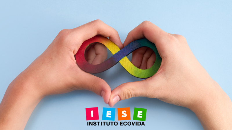 Símbolo da Neurodiversidade entre duas mãos em formato de coração representando a capado Curso Desvendando a Neurodiversidade do IESE Instituto Ecovida