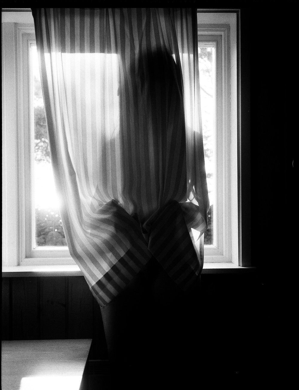 a black and white photo of a woman standing by the window behind a curtain from Lina Scheynius photo-essay for Tabayer jewelry