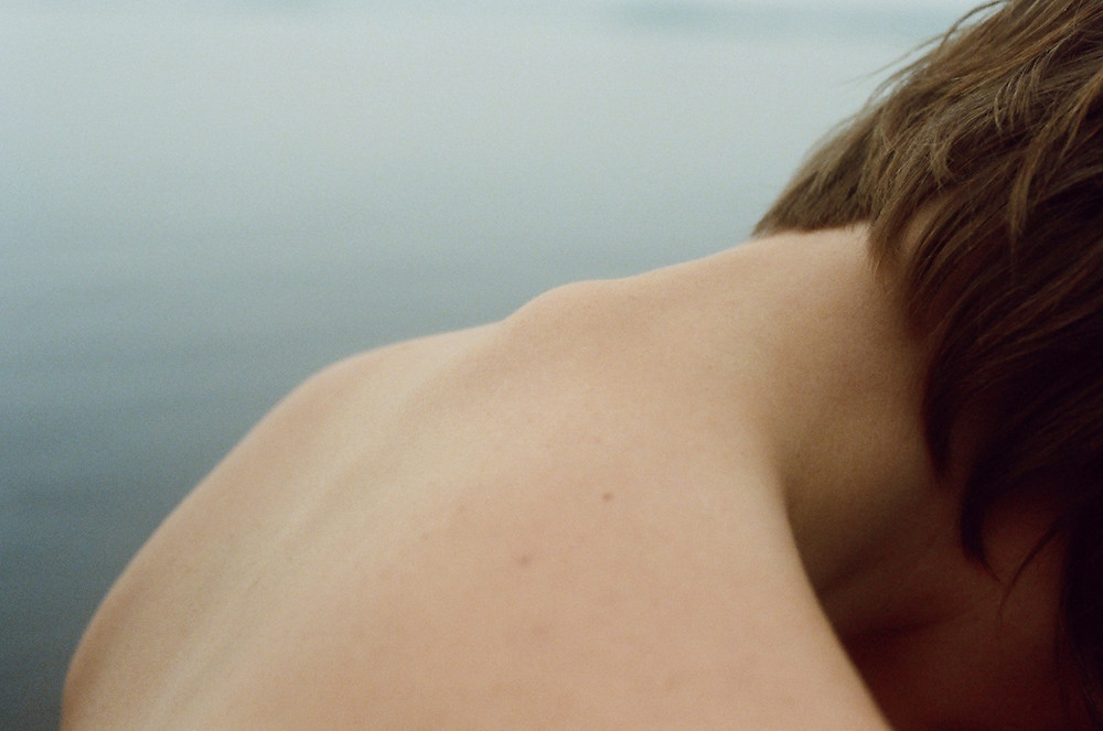 a photo of the back of the neck and spine of a woman with water in the background from Lina Scheynius photo-essay for Tabayer jewelry