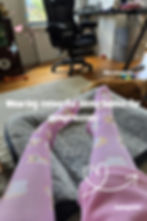 Feet in pink dog-patterned socks on a gray rug. A dog lounges nearby. Text reads, "Wearing colourful socks (bonus for compression)."