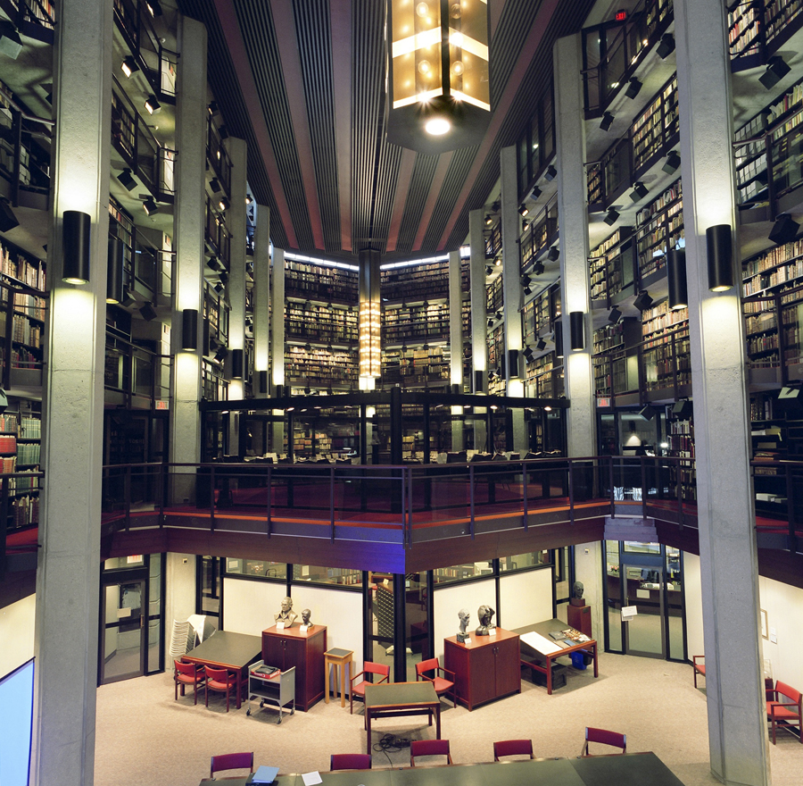 Grand circular library interior with tall book stacks, balcony railings, warm hanging lights, and EXIT signs; empty and quiet