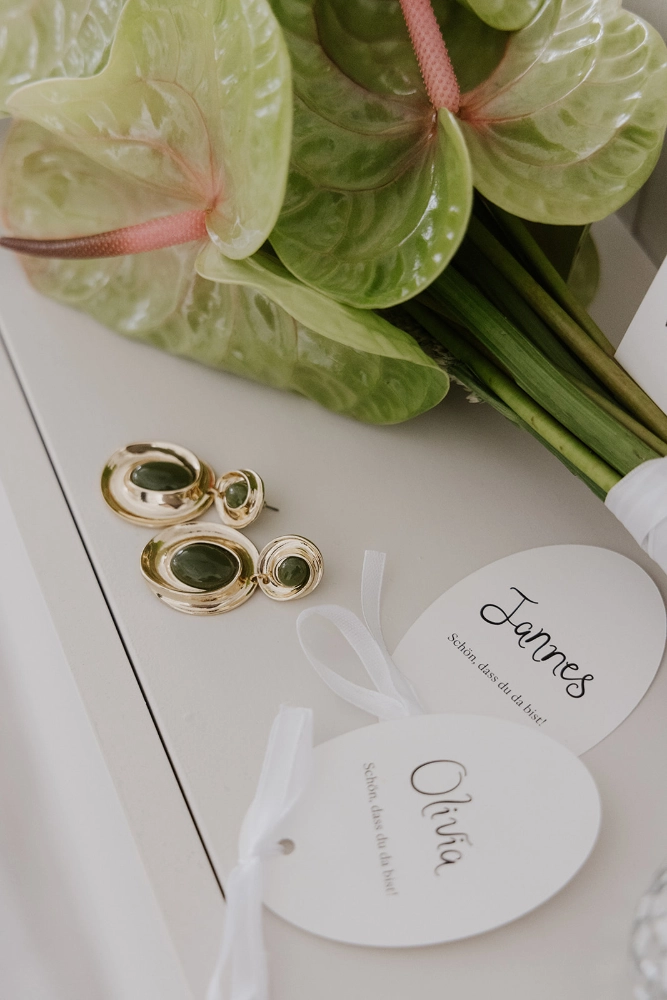 Elegante Namensanhänger für die Hochzeit mit filigraner Typografie, personalisiert für Gäste – kombiniert mit edlen Accessoires und einem modernen Brautstrauß für eine stilvolle Hochzeitsdekoration im Fine Art Stil.