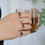 Thumbnail: model wearing a set of solid gold three stone gemstone rings and holding a coffee cup