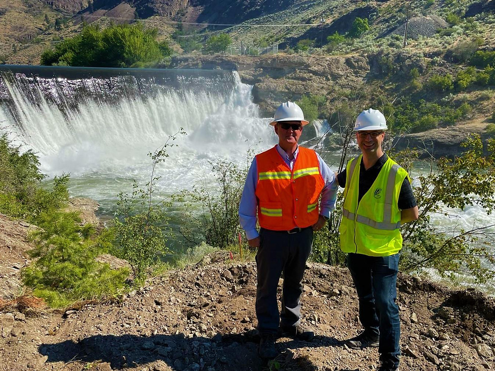 Two men are standing in front of the dam