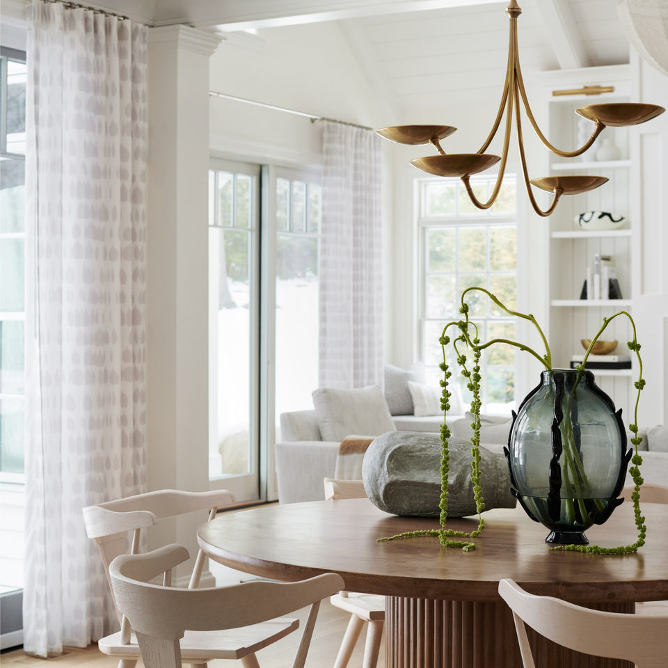 Wellesley dining area with round wood table, sculptural brass chandelier, patterned drapery, and white oak floors.