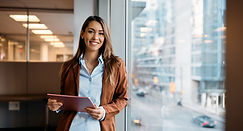 Young happy businesswoman using digital tablet while standing by the window in the office