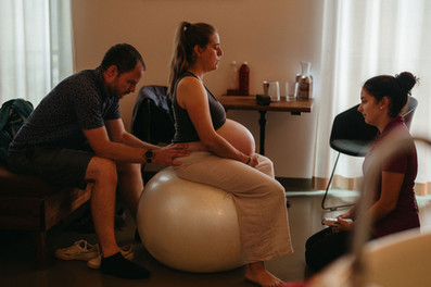 eine-gebaerende-sitzt-auf-einem-pezziball-mit-partner-und-hebamme-im-geburtshaus-geburtsfotografie-von-isabell-steinert-in-freiburg