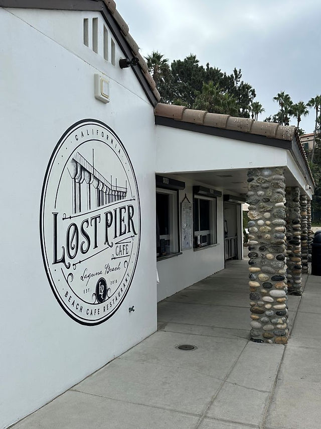 Lost Pier Cafe entrance at Aliso Beach in Laguna Beach, with the circular Lost Pier sign on the white exterior wall.