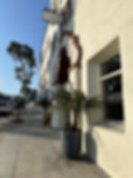 Sidewalk next to large white building with red arches over the door.