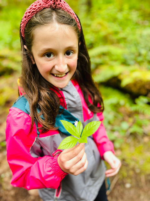 girl holding green leaves and a white flower