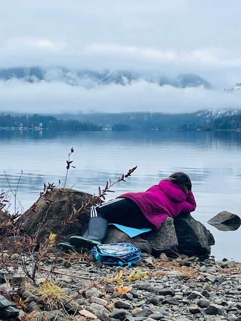 person laying on rock overlooking water and mountains