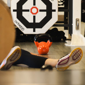 Orange kettlebell next to a persons that is laying on the floor. all you can see is their feet.