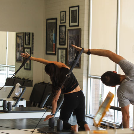 Man and woman doing a side reach movement on the Pilates Reformer