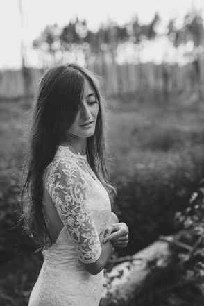 a black and white portrait of a bride, sanding on a meadow, trees in the background