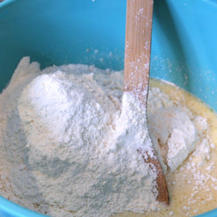 Flour added to melted butter in a blue bowl with a wooden spoon