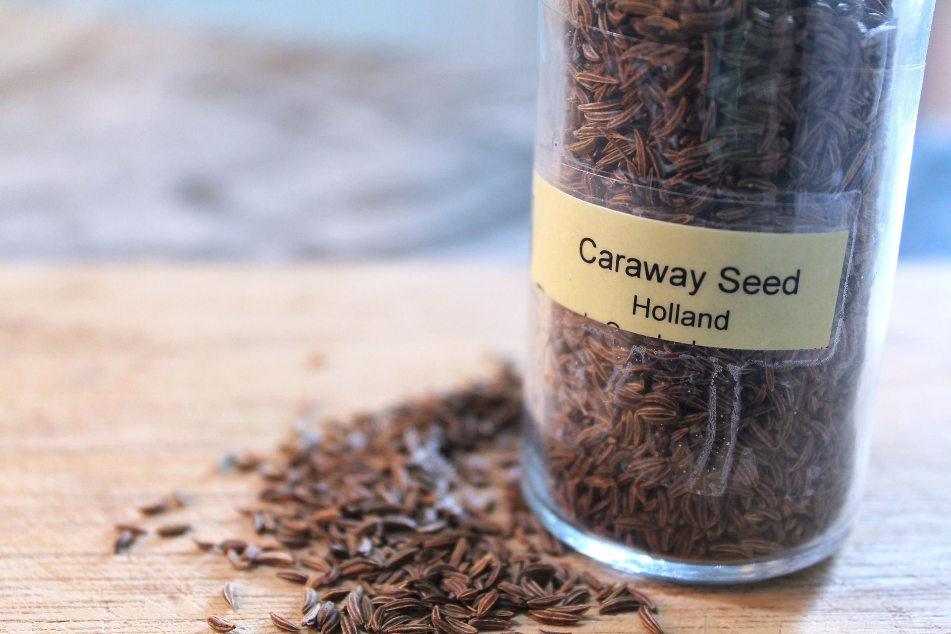 Pile of caraway seeds on a cutting board next to a jar that says "Caraway Seed Holland"