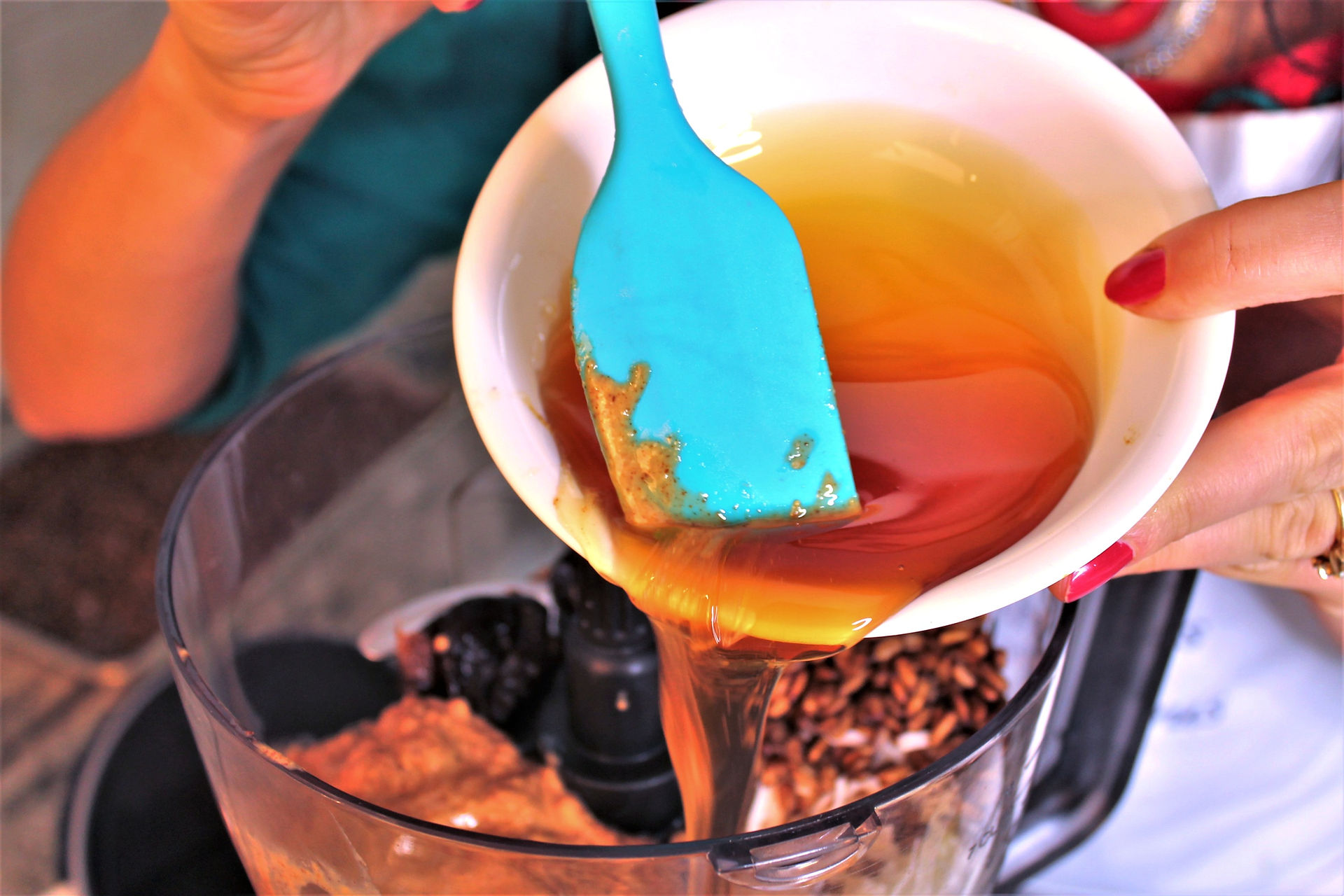 Bowl of honey being poured into a food processor with nuts and dates in it