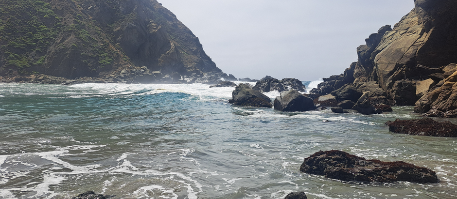 The ocean off the central Californian Coast, a green mountain on one side and a rocky outcrop on the other.