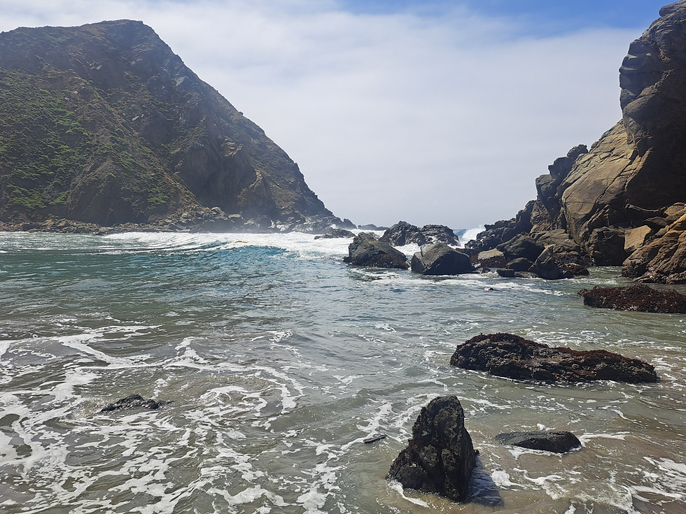 The ocean off the central Californian Coast, a green mountain on one side and a rocky outcrop on the other.
