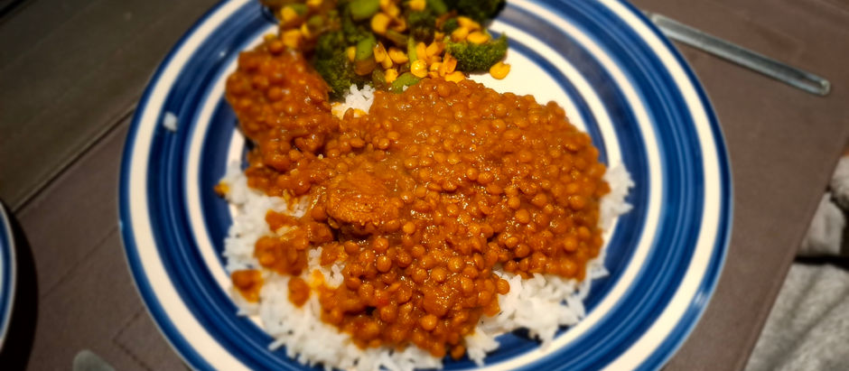 Plate of rice topped with lentil curry and a side of broccoli and corn. Dish served on a blue and white striped plate.