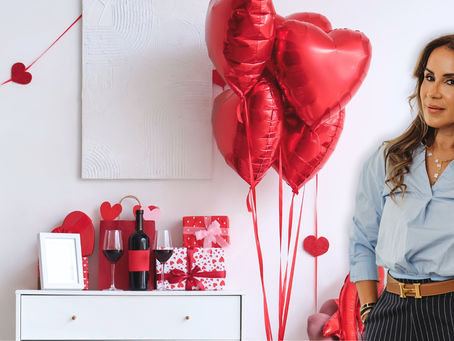 Michelle Herasme, Board-Certified Nurse Practitioner and founder of Herasme Beauty, standing in her Englewood, NJ studio decorated with red heart balloons and Valentine's Day gifts including wine, wrapped presents, and heart decorations