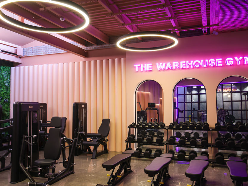 The Warehouse Gym Oranmore Ladies Section. Pink Neon sign saying 'The Warehouse Gym' along with dumbbells, mirrors and Gym Benches