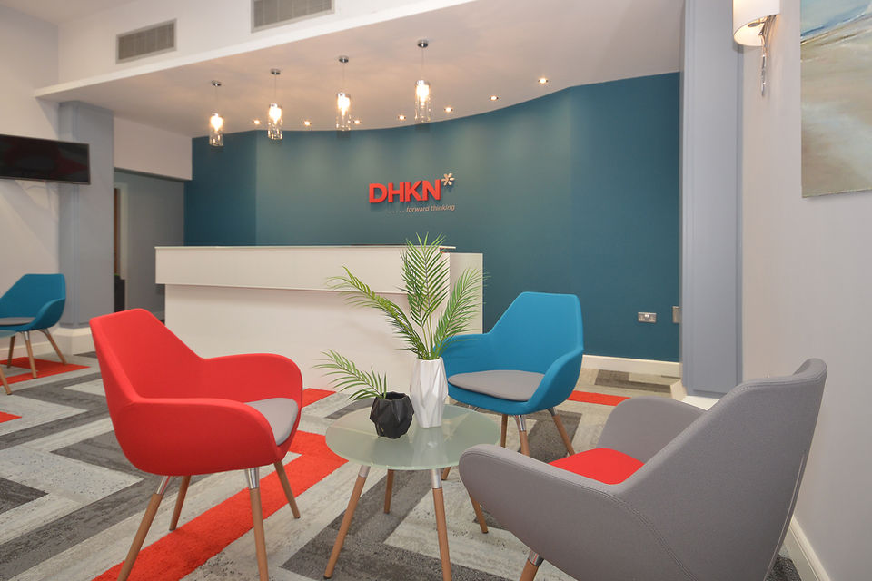 DHKN interior design for commercial office space. Red, white and grey geometrical carpet. Blue walls with red DHKN Logo and a white reception desk. Blue, red and grey seats to match.