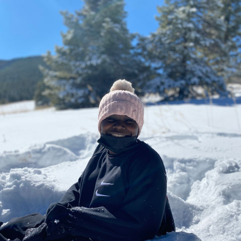 Smiling student in pink beanie sitting in snowy landscape