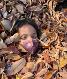 Child smiling, face in autumn leaves, wearing mask