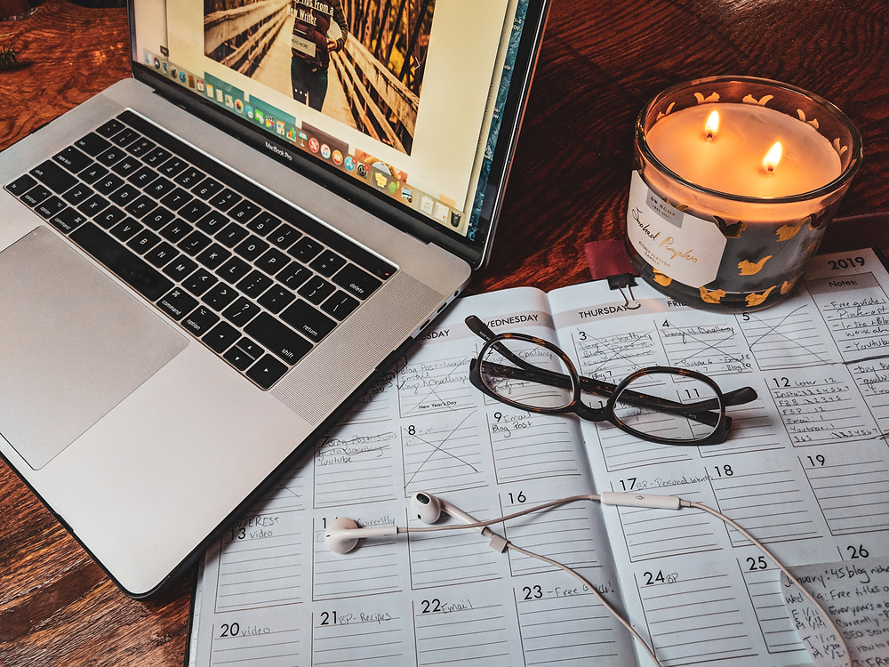 An image of a computer, planner, glasses, headphones, and a candle displayed as I get ready to write my next blog post.