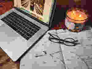 An image of a computer, planner, glasses, headphones, and a candle displayed as I get ready to write my next blog post.