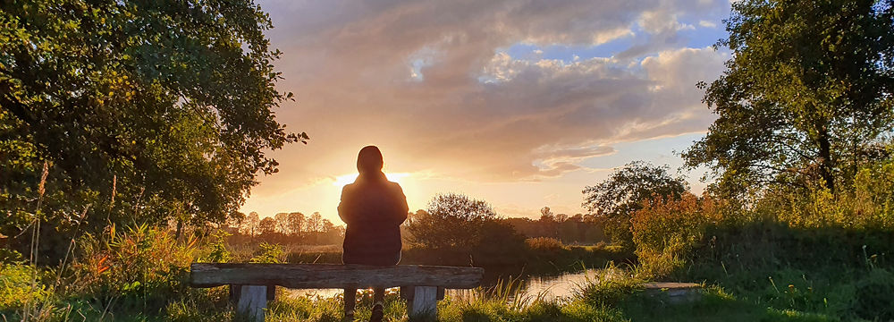 Woman sitting on a bench in a beautiful field, admiring the breathtaking sunset and enjoying a peaceful moment of wellness and self-care.